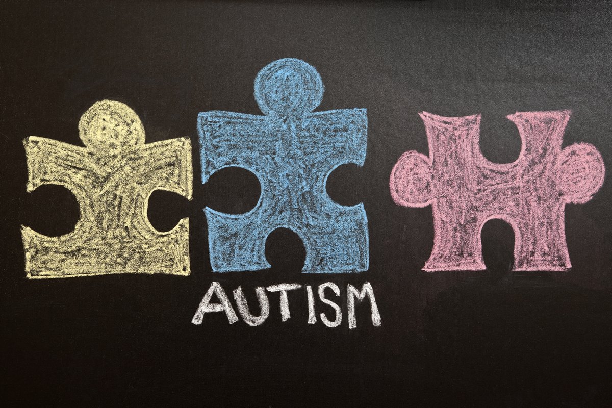 A yellow, blue and red puzzle pieces and the word Autism drawn on a chalkboard.